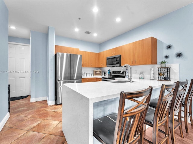 kitchen featuring sink, light tile patterned floors, kitchen peninsula, a breakfast bar area, and appliances with stainless steel finishes