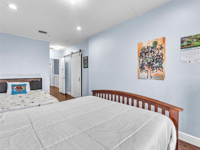 bedroom with a barn door and dark hardwood / wood-style floors