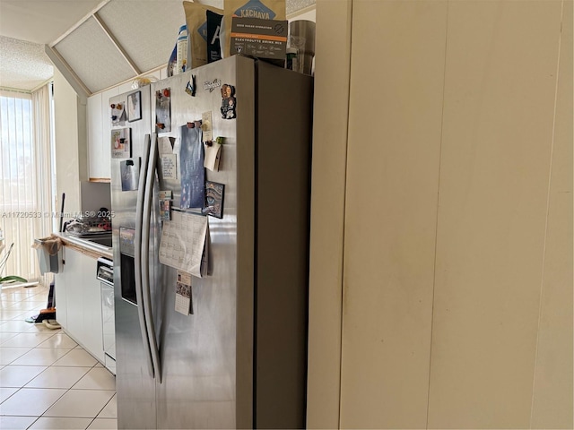 kitchen with lofted ceiling, white cabinets, light tile patterned flooring, and stainless steel fridge