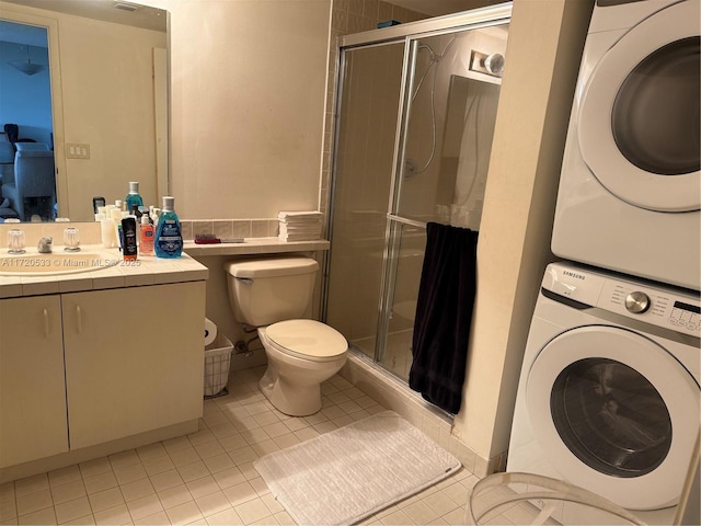 bathroom featuring toilet, stacked washing maching and dryer, tile patterned floors, an enclosed shower, and vanity