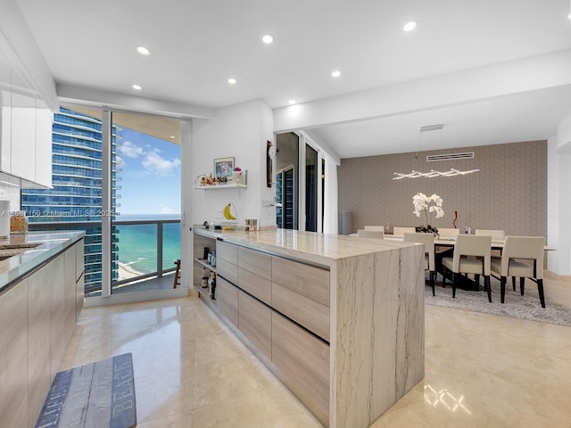 kitchen with a water view, light brown cabinetry, floor to ceiling windows, and light stone countertops