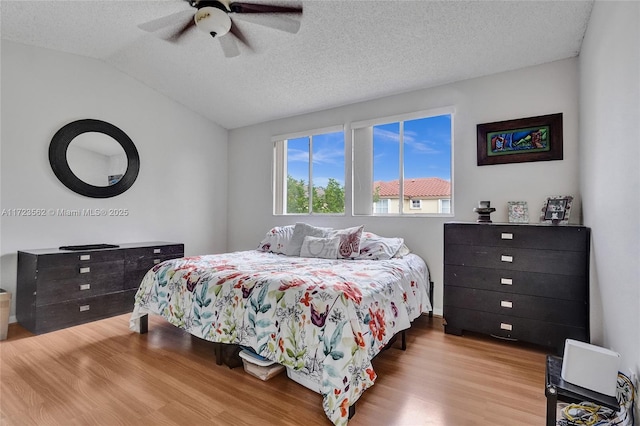 bedroom with lofted ceiling, ceiling fan, a textured ceiling, and light wood-type flooring