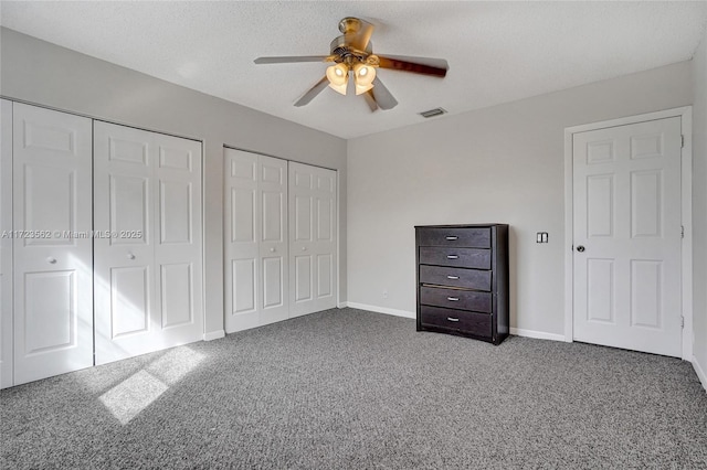 unfurnished bedroom featuring ceiling fan, two closets, a textured ceiling, and carpet