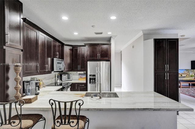 kitchen featuring appliances with stainless steel finishes, light stone counters, a textured ceiling, a kitchen bar, and kitchen peninsula