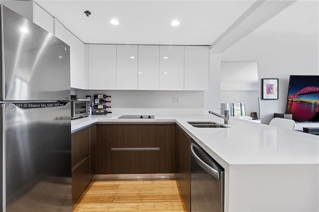 kitchen featuring stainless steel appliances, sink, white cabinets, kitchen peninsula, and dark brown cabinets