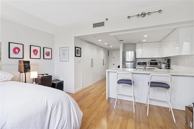 bedroom with sink, stainless steel refrigerator, and light wood-type flooring