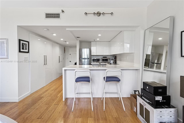 kitchen with light hardwood / wood-style floors, stainless steel appliances, kitchen peninsula, a breakfast bar, and white cabinets