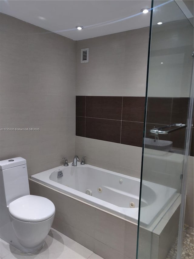 bathroom featuring toilet, tile patterned flooring, tile walls, and tiled tub