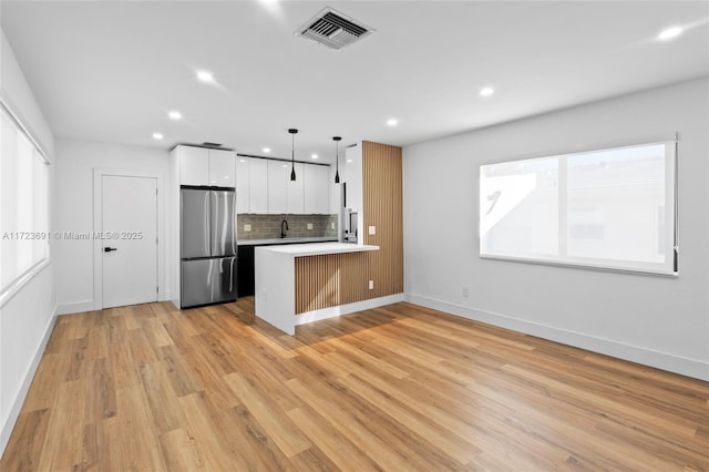 kitchen with hanging light fixtures, stainless steel refrigerator, kitchen peninsula, white cabinets, and backsplash