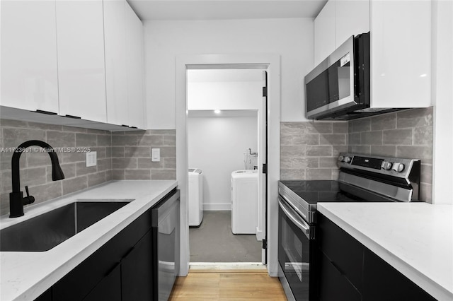 kitchen with appliances with stainless steel finishes, washer and dryer, sink, white cabinets, and light stone counters