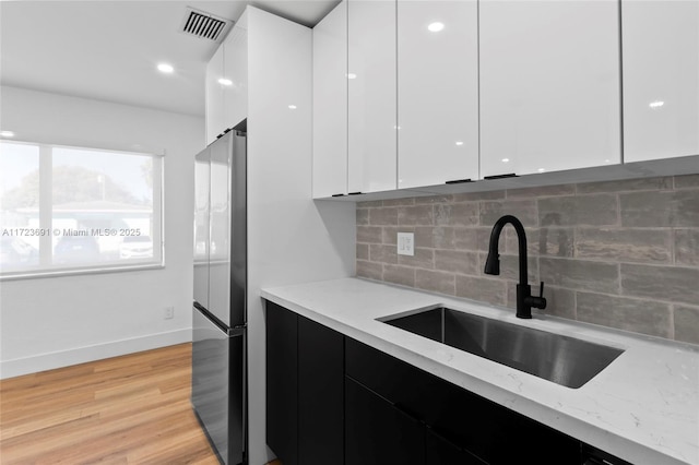 kitchen with sink, stainless steel fridge, light stone counters, light hardwood / wood-style floors, and white cabinets