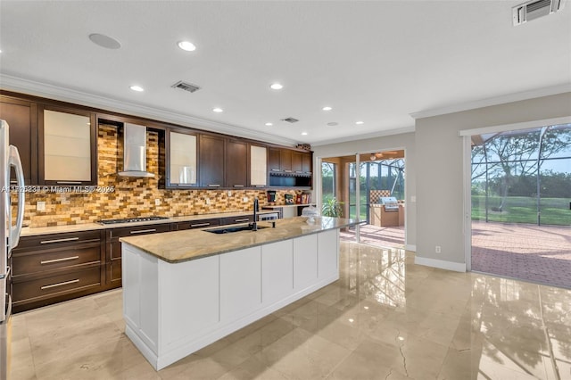 kitchen featuring an island with sink, stainless steel gas stovetop, wall chimney exhaust hood, and backsplash