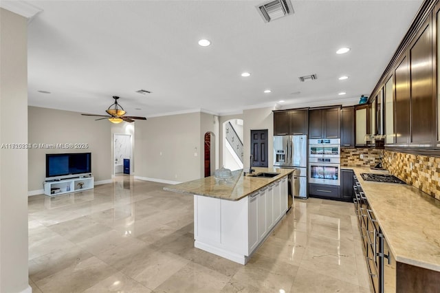 kitchen featuring light stone countertops, stainless steel appliances, a center island with sink, backsplash, and dark brown cabinets