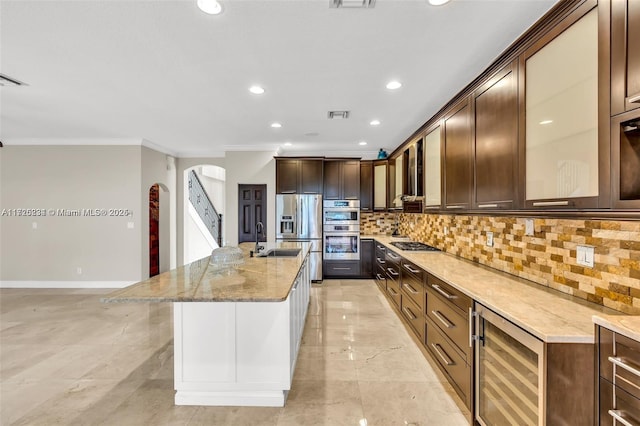 kitchen featuring sink, ornamental molding, beverage cooler, a center island with sink, and appliances with stainless steel finishes