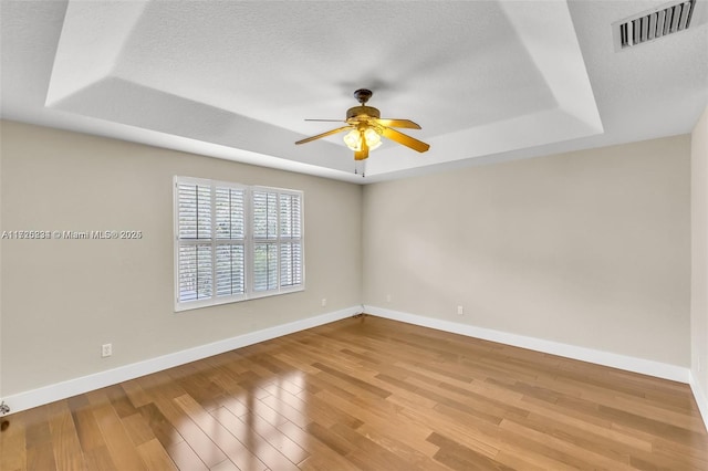 empty room with a raised ceiling, a textured ceiling, ceiling fan, and light hardwood / wood-style floors