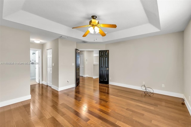 empty room with a raised ceiling, ceiling fan, and hardwood / wood-style flooring