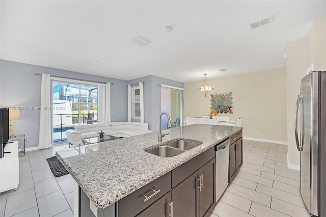 kitchen with light stone countertops, stainless steel appliances, a center island with sink, a notable chandelier, and sink