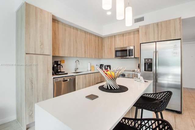 kitchen featuring sink, stainless steel appliances, decorative light fixtures, and light brown cabinets