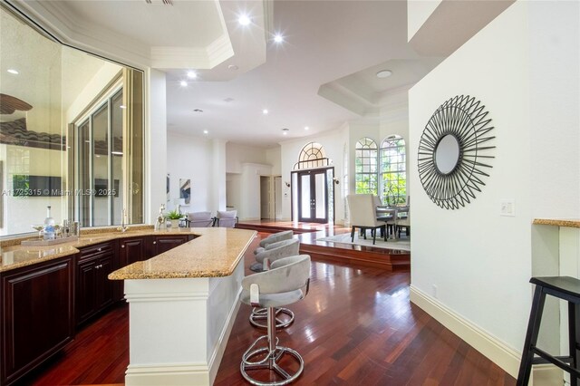 kitchen featuring dark wood-style floors, light stone counters, a breakfast bar area, open floor plan, and crown molding