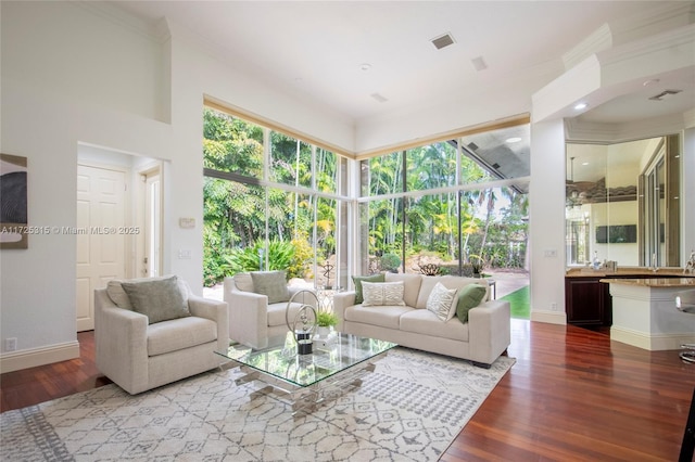 living room featuring ornamental molding, visible vents, baseboards, and wood finished floors