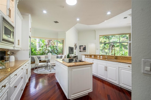 kitchen with dark wood-type flooring, a center island, white cabinetry, light stone countertops, and stainless steel microwave