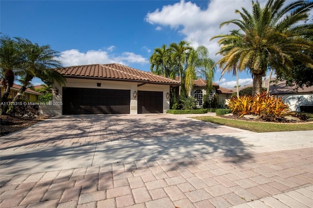 mediterranean / spanish-style house with a garage, decorative driveway, a tile roof, and stucco siding