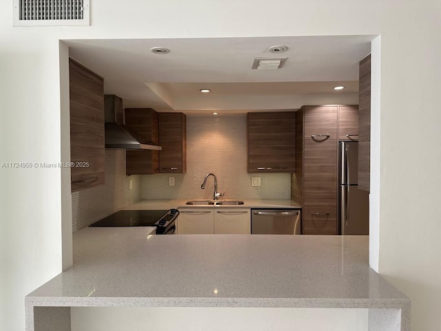 kitchen featuring light stone countertops, wall chimney exhaust hood, decorative backsplash, appliances with stainless steel finishes, and sink