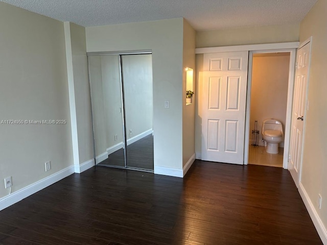 unfurnished bedroom featuring a textured ceiling, connected bathroom, a closet, and dark hardwood / wood-style floors