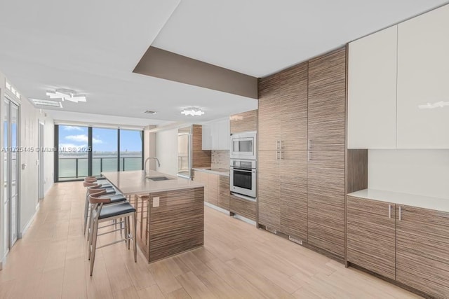 kitchen featuring sink, a breakfast bar, appliances with stainless steel finishes, white cabinetry, and a kitchen island with sink