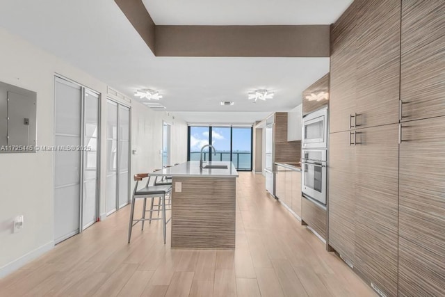 kitchen with a breakfast bar, appliances with stainless steel finishes, electric panel, an island with sink, and expansive windows