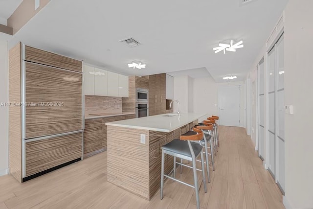 kitchen with sink, white cabinetry, appliances with stainless steel finishes, a kitchen breakfast bar, and an island with sink