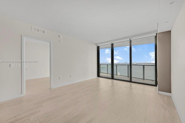 empty room with light wood-type flooring and a wall of windows