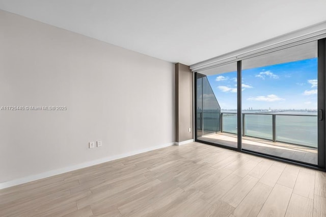 unfurnished room with a water view, a wall of windows, and light wood-type flooring