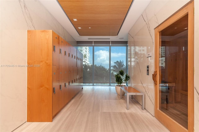 hall featuring light wood-type flooring, wooden ceiling, and a wall of windows