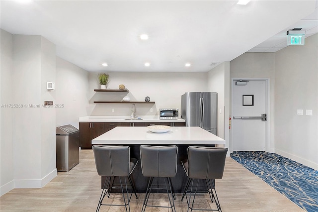 kitchen with a kitchen breakfast bar, a center island, stainless steel refrigerator, and light wood-type flooring