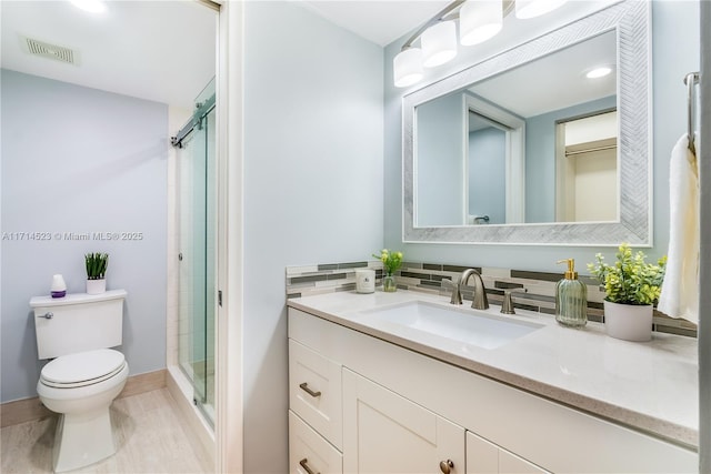 bathroom featuring a shower with door, vanity, and toilet