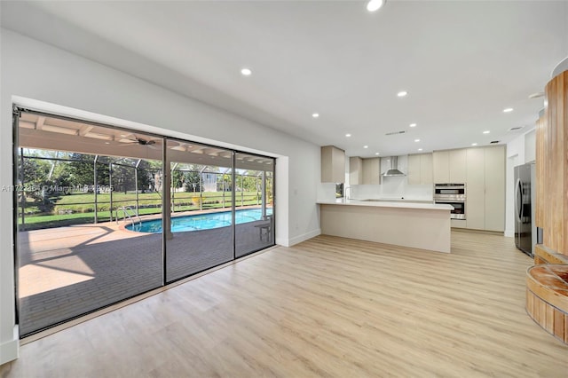 kitchen with kitchen peninsula, wall chimney range hood, light hardwood / wood-style floors, and plenty of natural light