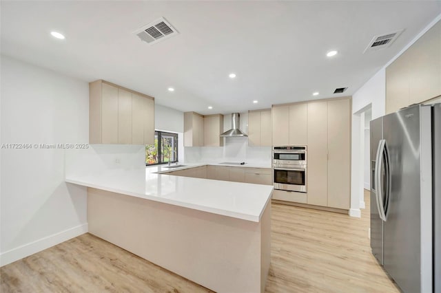 kitchen with appliances with stainless steel finishes, light wood-type flooring, kitchen peninsula, and wall chimney exhaust hood