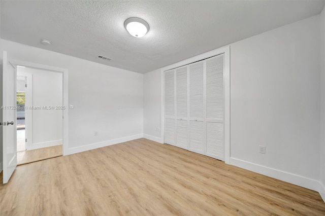 unfurnished bedroom featuring a textured ceiling, light wood-type flooring, and a closet