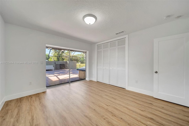 unfurnished bedroom featuring a closet, access to exterior, light wood-type flooring, and a textured ceiling