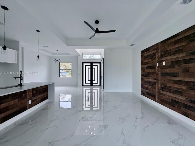 interior space featuring ceiling fan, wooden walls, a tray ceiling, and hanging light fixtures