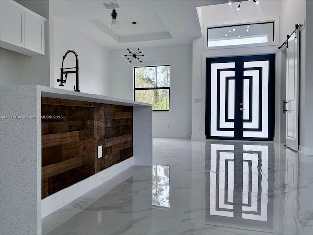 entryway with an inviting chandelier, french doors, a tray ceiling, and a barn door