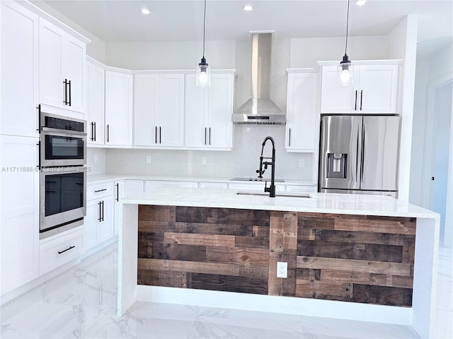 kitchen featuring wall chimney exhaust hood, hanging light fixtures, tasteful backsplash, white cabinetry, and appliances with stainless steel finishes