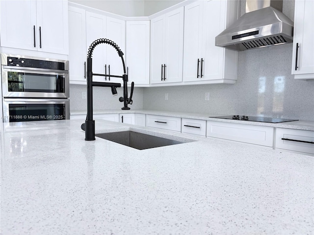 kitchen featuring black electric stovetop, white cabinets, wall chimney range hood, and light stone countertops