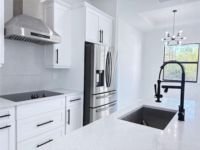 kitchen with light stone counters, wall chimney range hood, stainless steel refrigerator with ice dispenser, white cabinetry, and sink