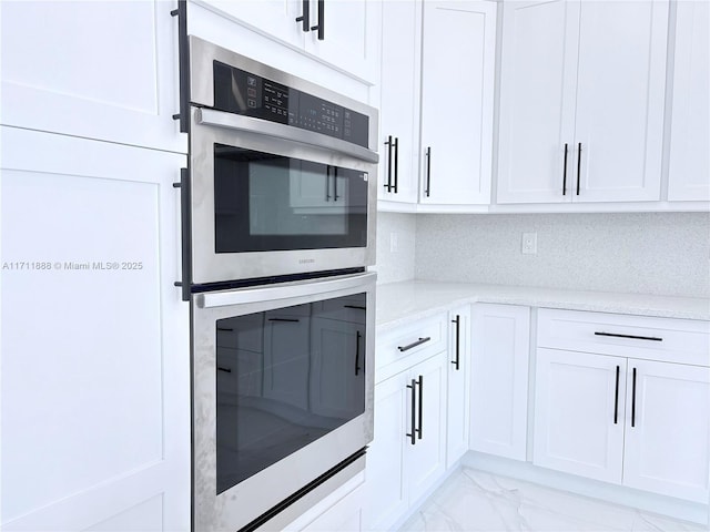 kitchen with double oven, white cabinetry, light stone counters, and decorative backsplash