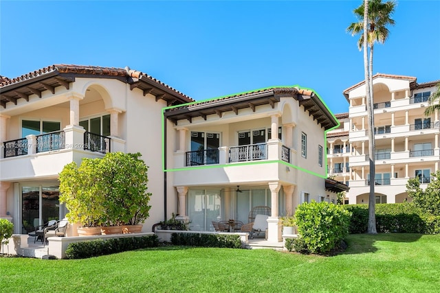 rear view of house with a balcony, a lawn, and a patio