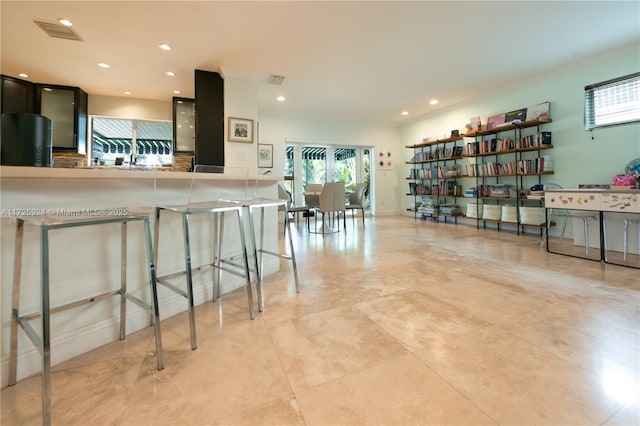 kitchen featuring kitchen peninsula, fridge, ornamental molding, and a kitchen bar