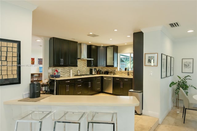 kitchen featuring kitchen peninsula, wall chimney exhaust hood, a kitchen bar, backsplash, and appliances with stainless steel finishes