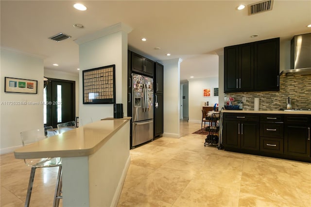 kitchen featuring a kitchen breakfast bar, crown molding, stainless steel fridge, wall chimney exhaust hood, and tasteful backsplash